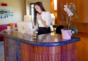 a woman talking on a phone at a desk with a laptop at Hotel La Fenice in Lignano Sabbiadoro