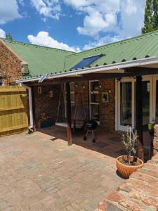una casa in mattoni con un tetto verde e un patio di Palmboom Cottage at Sielerus by Horeb a Clarens