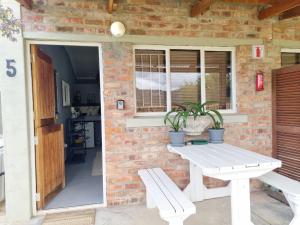 a white picnic table and a bench in front of a brick wall at Amanzi Farm Rooms in Montagu