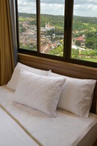 a bed with white pillows in front of a window at Pousada Da Serra in Bananeiras