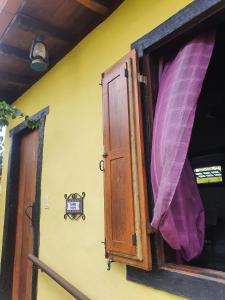 a window with a purple curtain on a yellow wall at Pousada Villa di Lavras in Lavras Novas