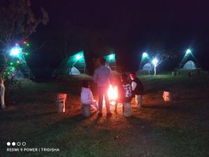 a group of people standing around a fire at night at Fesengbor eco camp in Kāziranga +4 photos