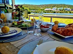 a wooden table with plates of food and wine glasses at A Rickety River House in Stilbaai