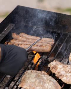 una persona che cucina salsicce su una griglia con una spatola di Chalet Al Maso Val Calamento a Telve