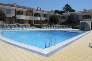 Una gran piscina con sillas y un edificio. en Villaggio Tulipano, en Bibione