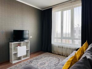 ein Wohnzimmer mit einem Sofa, einem TV und einem Fenster in der Unterkunft Солнечная квартира на высоком этаже in Almaty