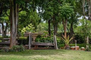 una panchina di legno in un parco con alberi e piante di Jaris Cottage a Nong Nam Daeng Altre 6 foto