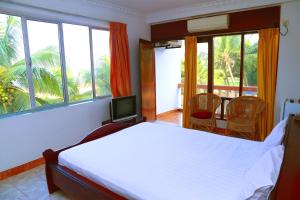 a bedroom with a bed and a television and windows at Topaz Beach Hotel in Negombo
