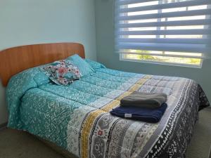 a bed with a quilt on it with a window at Depto Montserrath en Condominio 3D 1B Parking Excelente Conectividad, Atención Empresas-Facturas in Chillán