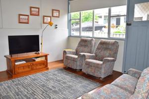 a living room with two chairs and a flat screen tv at Sunshine Cottage - Bring your own linen. in South West Rocks