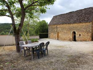 Charmante maison rustique en pierres, proche de Sarlat - FR-1-616-385 في Marcillac-Saint-Quentin: طاولة وكراسي تحت شجرة بجوار مبنى
