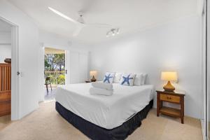 a white bedroom with a bed and a balcony at Serenity Apartments Noosa in Noosa Heads