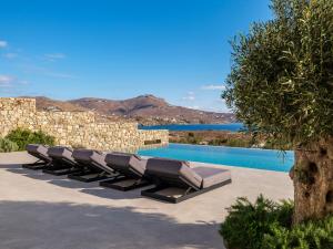a row of lounge chairs next to a swimming pool at Amnos Mykonos - A Blue Eye Collection Villa in Kalafatis