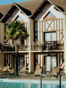 a building with chairs and a palm tree next to a pool at Logis Le Clos Deauville Saint Gatien in Saint-Gâtien-des-Bois