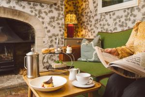 a woman reading a book in a living room with a fireplace at The Swan Hotel in Bibury