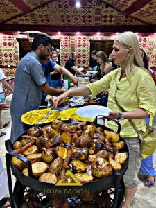 a woman is standing next to a grill with food at Rum Moon Bubbles Luxury Camp in Wadi Rum