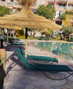eine Gruppe von Liegestühlen und einem Sonnenschirm neben einem Pool in der Unterkunft Harmonie d Agdal Marrakech avec Piscine in Marrakesch