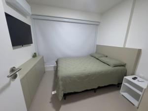ein kleines weißes Schlafzimmer mit einem Bett und einem TV in der Unterkunft Apartamento em Recife, condomínio de luxo in Recife
