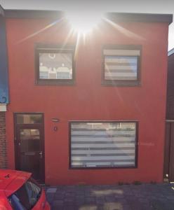 a red building with two windows and a car parked in front at Smile Home Wijk aan Zee 1 in Wijk aan Zee