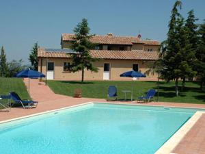 a swimming pool in front of a house with chairs and umbrellas at Agriturismo L'Imposto in Pomarance