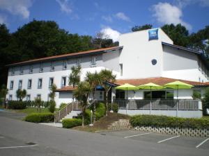 un bâtiment blanc avec des parasols verts dans un parking dans l'établissement IBIS BUDGET Biarritz - Anglet, à Anglet