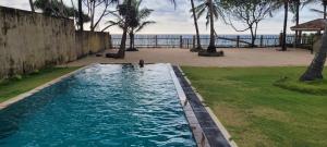 a swimming pool next to a beach with palm trees at Olu Beach Villa in Ambalangoda