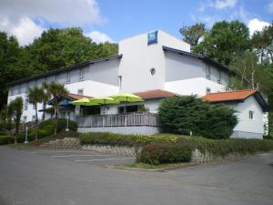 a white building with green umbrellas in a parking lot at IBIS BUDGET Biarritz - Anglet in Anglet