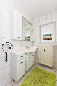 a white bathroom with a sink and a green rug at Haus Kajedeich FeWo Seestern in Bensersiel