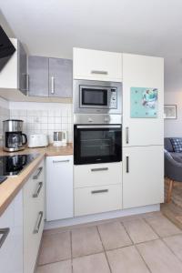 a kitchen with white cabinets and a microwave at Haus Kajedeich FeWo Robbe in Bensersiel +9 photos