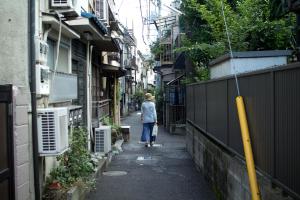 a woman walking down a narrow alley with buildings at hanare in Tokyo
