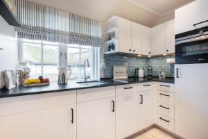 une cuisine avec des armoires blanches et des comptoirs noirs dans l'établissement Ferienwohnung Luettje Moehl - Kleines Paradies am Wattenmeer in Keitum Sylt, à Keitum