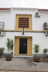 a white building with a black door and two plants at Hospedaria A Italiana in Moura
