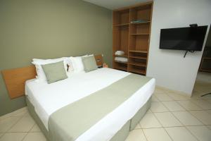 a bedroom with a large white bed with a flat screen tv at Hotel Sesi Aruana in Aruanã