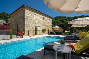 a swimming pool with chairs and an umbrella next to a building at Casa Zé Manel - Turismo Rural in Paranhos