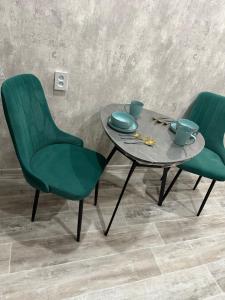 a table with two green chairs and a table with cups at Двухкомнатная уютная квартира in Ekibastuz
