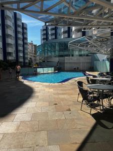 a swimming pool with tables and chairs in a building at Águas da Serra - Apto 2qts in Rio Quente