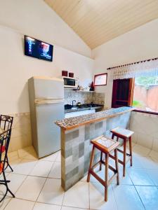 Una cocina con refrigerador y una encimera con taburetes. en Vilamaruá Chalé próximo da praia do Perequê, en Ilhabela