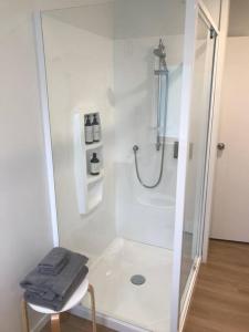 a white bathroom with a shower with a glass door at Manuka Cottage Oneroa in Waiheke Island +1 photo