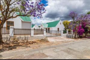 a white house with a fence and purple trees at De Rust Karoo Cottages in De Rust