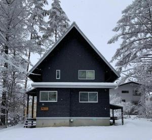 a black house in the snow with trees at Hakuba Cottage ICHIZAEMON by Jade Group in Hakuba