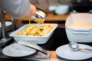 a person is pouring food into a bowl of food at Amenity Hotel & Resort Lipno in Lipno nad Vltavou