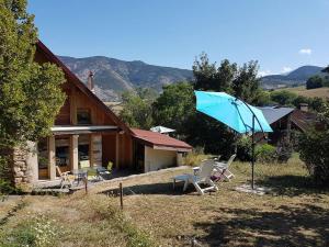 a house with a blue umbrella and chairs in front of it at Gîte La Sittelle in Bellaffaire