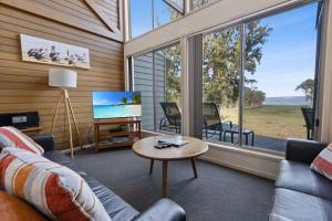 Una sala de estar con un sofá y un televisor y ventanas. en Steamer - Waterfront Retreat, en Goon Nure