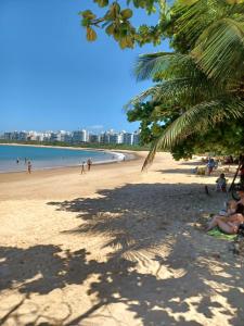 a beach with a palm tree and people on it at Novidade na Enseada Azul! Apto com churrasqueira, área gourmet e Ar condicionado a 150m da praia in Guarapari