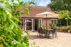 The Cow Barn - Norfolk Cottage Agency في Banningham: طاولة وكراسي مع مظلة أمام المنزل