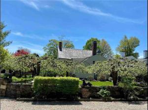a white house with a stone wall and trees at The Doctor 1781 House on the Litchfield Green in Litchfield