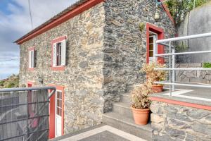 a stone house with a red door and stairs at Ocean View Cottage a Home in Madeira in Fajã da Ovelha