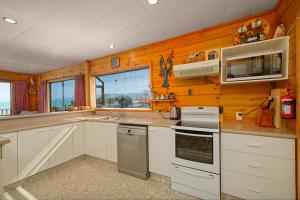 カイコウラにあるA Classic Kiwi Bach in South Bayの白いキャビネットと木製の壁が備わるキッチン