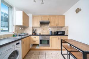 La cuisine est équipée de placards en bois, d'un évier et d'un lave-vaisselle. dans l'établissement Warm & Cosy Flat in King Cross, à Londres