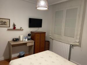 a bedroom with a bed and a television and a desk at Habitación con baño privado y jardín Cerca de las playas in Boó de Piélagos